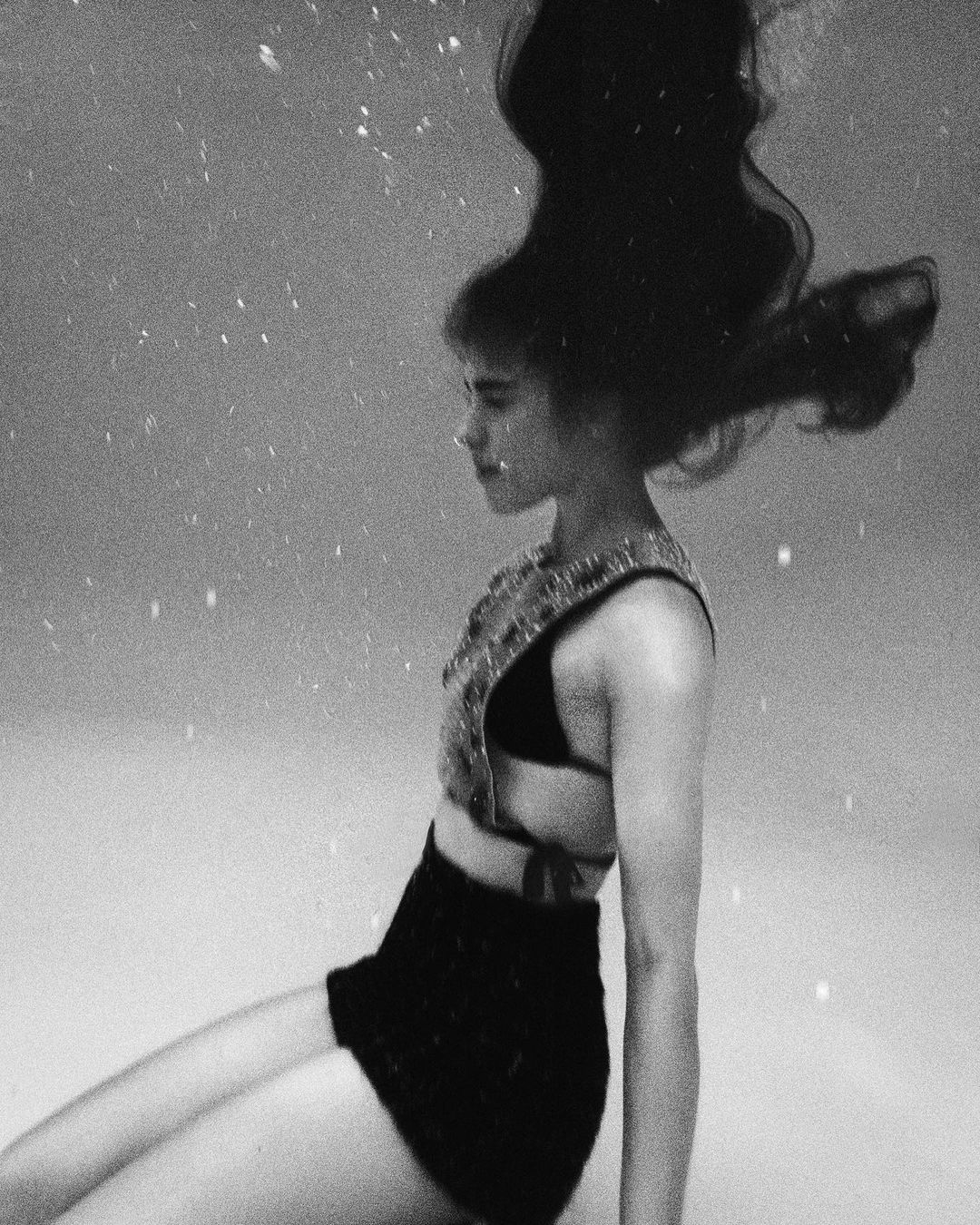 Monochrome underwater portrait of an adult female in a decorative top and black skirt, her hair floating around her in a serene scene.