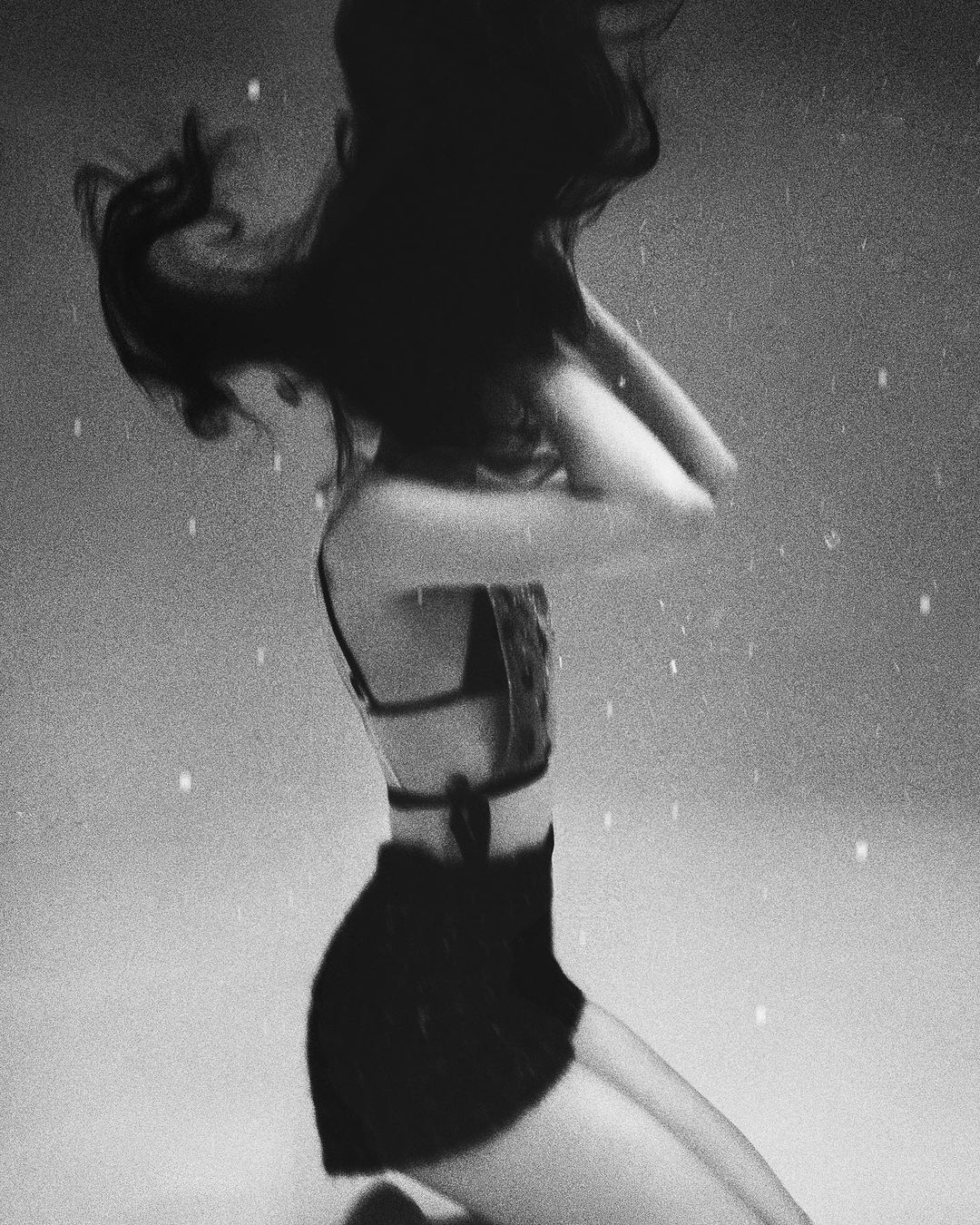 Black and white studio shot of a woman in a black two-piece kneeling in water, her long dark hair flowing around her head and shoulders.