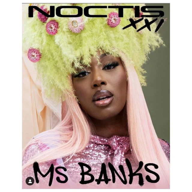 Dark-skinned woman with decorative headpiece and pink wig poses in a shiny pink top against a green and peach backdrop. 'Ms Banks' text.