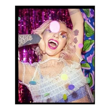 Blonde woman with confetti, wearing a white top and open mouth, in front of a purple and blue patterned background.