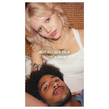 Close-up portrait of a blonde woman resting her head above a man with dark curly hair against a woven rattan background.