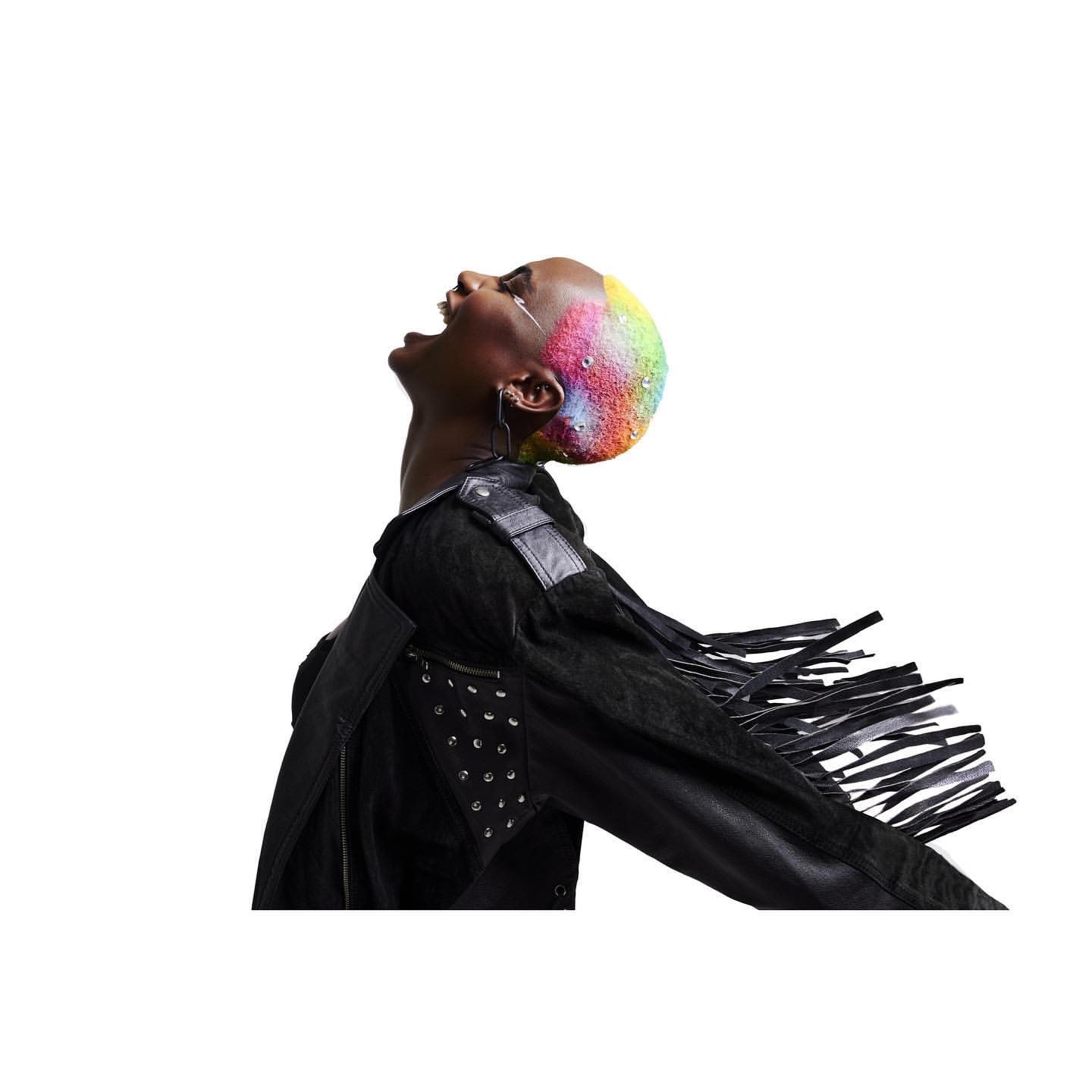Person with rainbow hair wearing a black jacket looking up with an open mouth in a minimalist white background studio shot