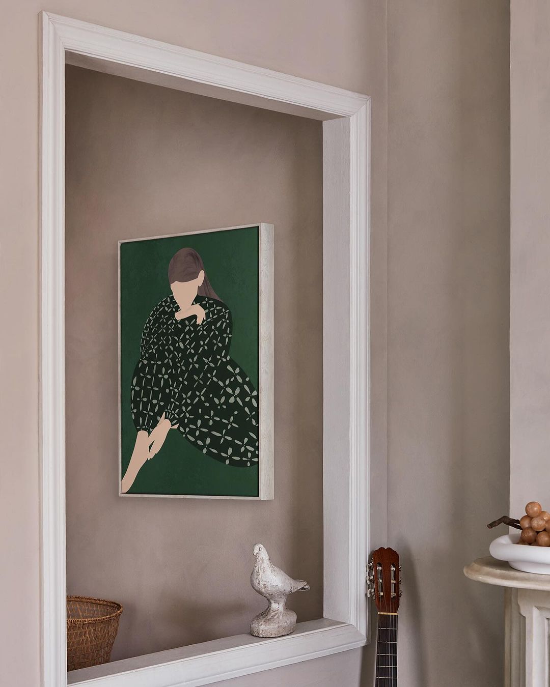 Illustration of a woman in green dress hanging on a wall above a decorative shelf with a white ceramic bird and small guitar. 