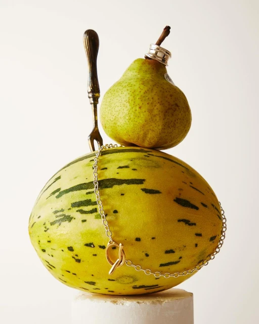 Still life featuring a pear and melon topped with rings and a fork, showcasing a playful blend of culinary and fashion elements.