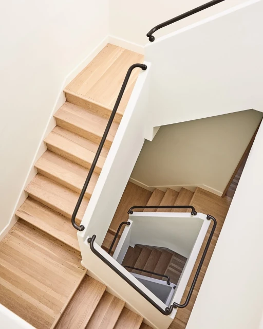 Interior view of a modern staircase with wooden steps and black metal railing. High-angle shot looking down the stairwell.