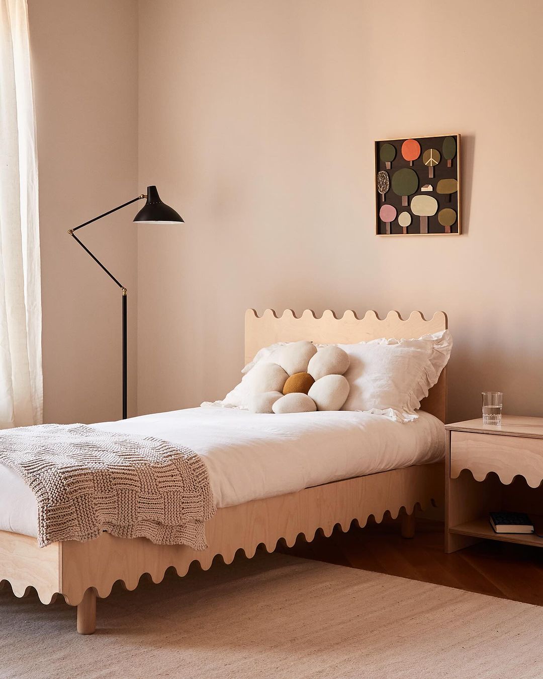 Bedroom interior featuring a wooden bed with white linens, a flower-shaped pillow, and an art piece on the wall, creating a cozy atmosphere.