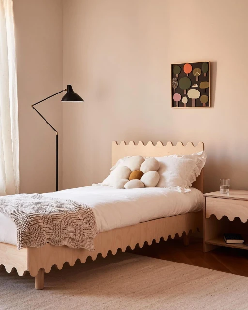 Bedroom interior featuring a wooden bed with white linens, a flower-shaped pillow, and an art piece on the wall, creating a cozy atmosphere.