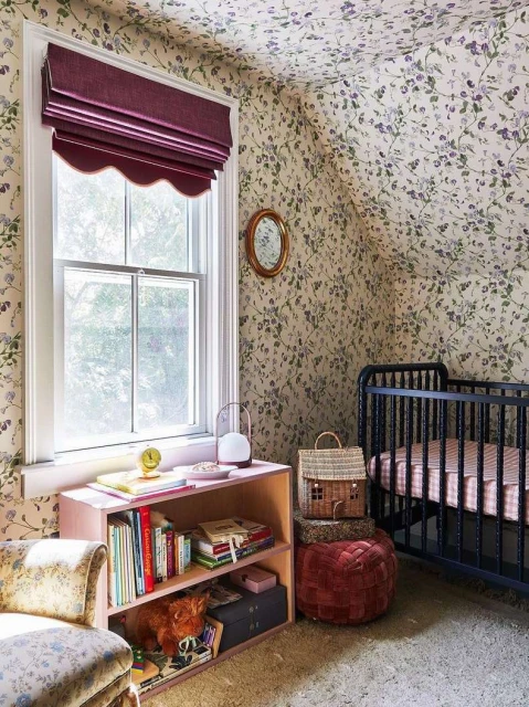 Cozy kid's room with floral wallpaper, crib, and pink bookshelf filled with books and toys, illuminated by natural light.