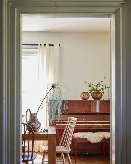 Interior view of a dining room with a table and chairs, a piano in the background, and natural light coming through a window.