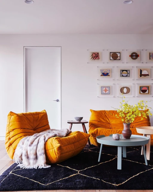 Living room interior featuring a mustard yellow Togo sofa and armchair, a dark geometric rug, and minimalist wall art in a brightly lit space.