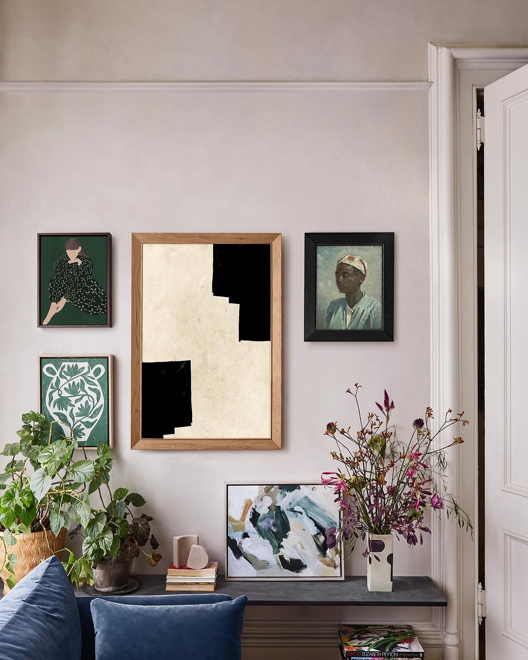 Interior wall featuring framed art including paintings and prints, a modern console table with decorative plants, flowers, and art books.