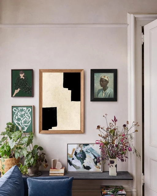 Interior wall featuring framed art including paintings and prints, a modern console table with decorative plants, flowers, and art books.