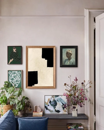 Interior wall featuring framed art including paintings and prints, a modern console table with decorative plants, flowers, and art books.