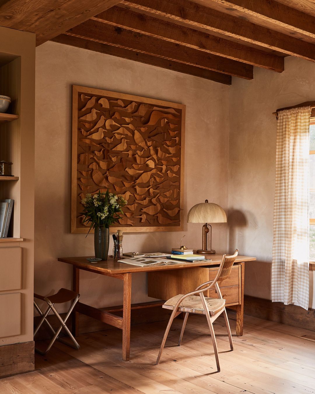 Well-lit home office interior featuring a wooden desk, chair, lamp, and decorative wall art, creating a warm and inviting workspace.