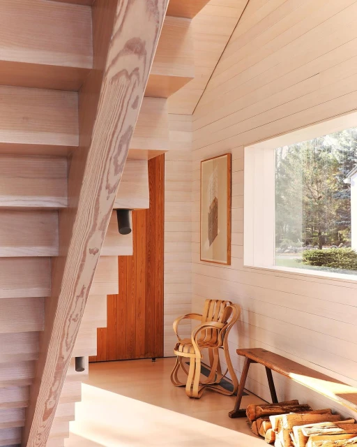 Interior view of a modern home with a light wood staircase, accent chair, bench, and window with natural light in a minimalist design.