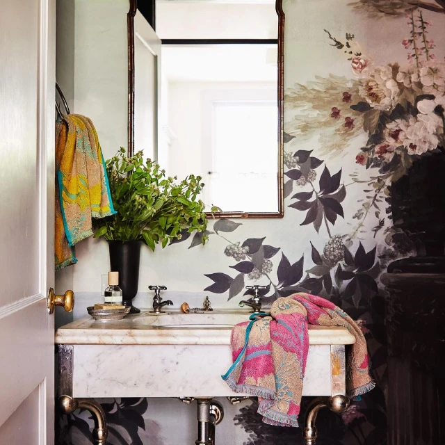 Bathroom interior featuring a marble sink, mirror, floral wallpaper, and colorful towels creating a bright and decorative space.