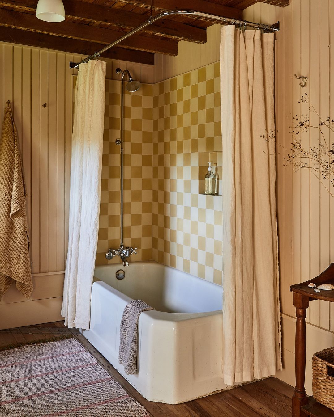 Bathroom interior featuring a white bathtub with a neutral-tone shower curtain, checkered tile wall, and wooden accents for a warm and inviting space.