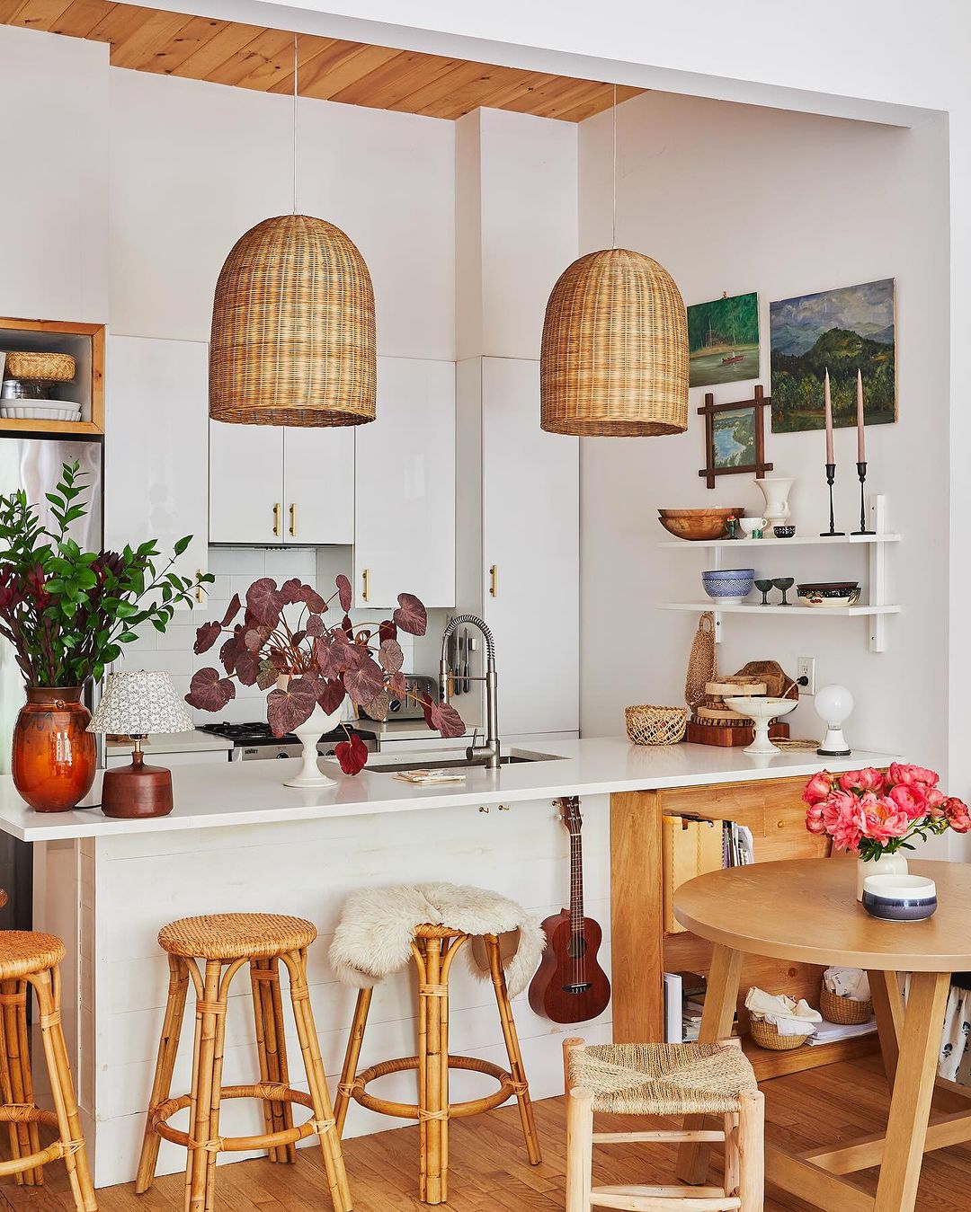Light and airy kitchen interior featuring wicker pendant lights, bamboo stools, a round wooden table, and white cabinetry.