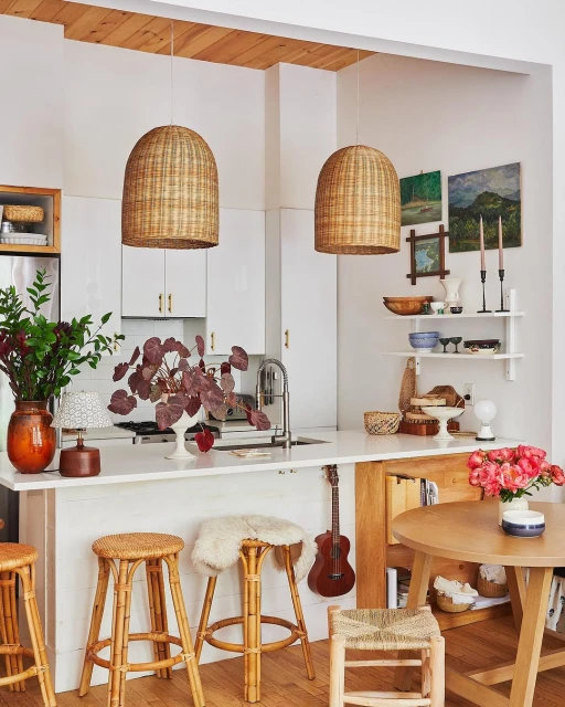 Light and airy kitchen interior featuring wicker pendant lights, bamboo stools, a round wooden table, and white cabinetry.