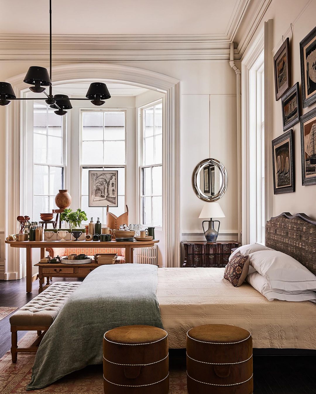 Bedroom interior with a bed styled with white linens and a light-colored throw. Brown upholstered ottomans at the foot of the bed.