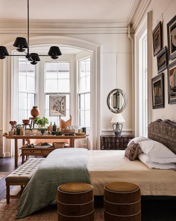 Bedroom interior with a bed styled with white linens and a light-colored throw. Brown upholstered ottomans at the foot of the bed.