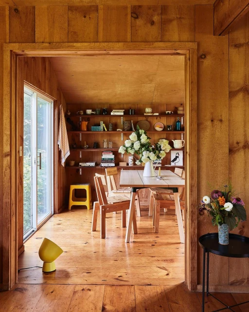 Cozy wood-paneled dining room with table set for a meal, featuring a floral centerpiece, open shelving, and a yellow floor lamp.