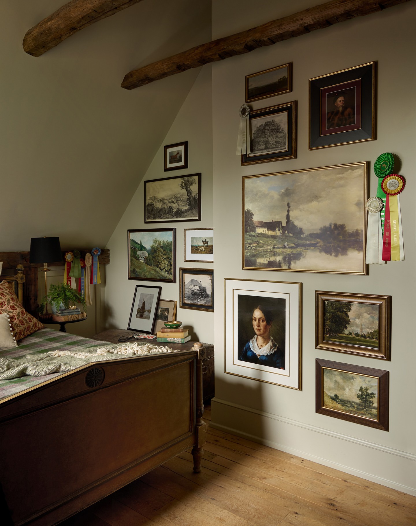 Interior bedroom view featuring an antique wooden bed, wood floors, beige walls, and a gallery wall of framed art and rosettes.