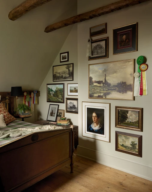 Interior bedroom view featuring an antique wooden bed, wood floors, beige walls, and a gallery wall of framed art and rosettes.