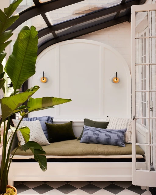Indoor nook with pillows on a bench, a large plant in a pot, and a black and white checkered floor creates a cozy, relaxing space.