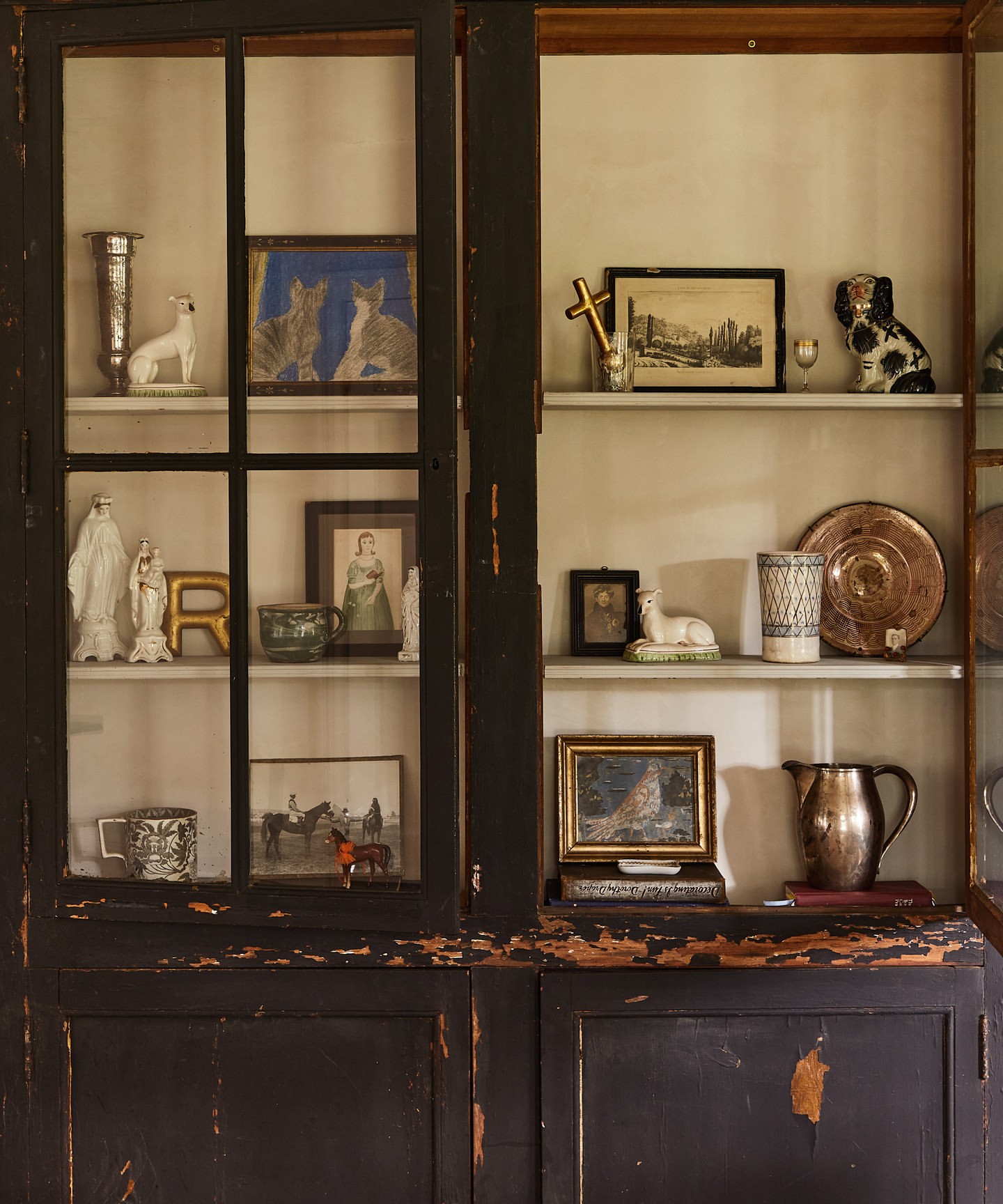 Antique cabinet with glass doors displays a collection of decorative objects and pictures on shelves, creating a vintage interior scene.