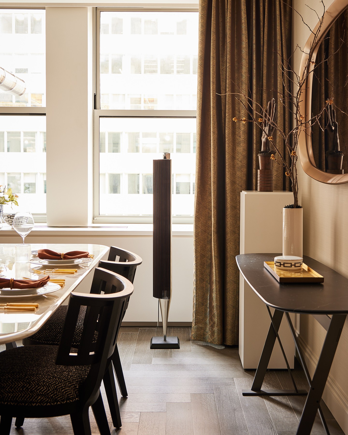 Dining room features a marble-top table with place settings, flanked by black chairs and a tall speaker, complemented by neutral decor and lighting.
