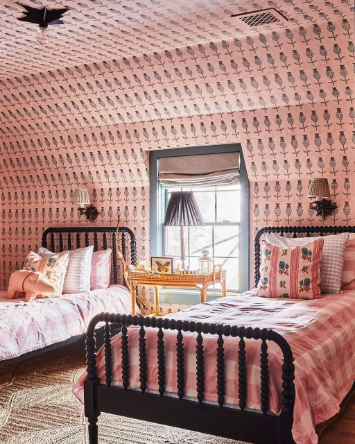 Bedroom interior with two black spindle beds, pink floral wallpaper, table with a butterfly display, and a woven rug.