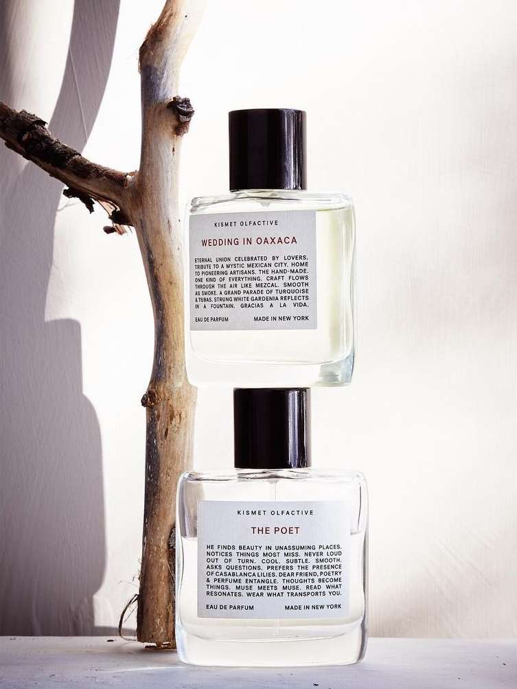 Two Kismet Olfactive perfume bottles stacked next to a branch, soft lighting, minimalist design. Ideal for beauty or product advertising.