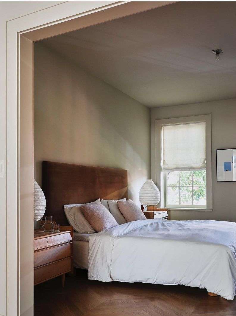 Bedroom interior with a bed featuring a brown headboard, white bedding, a wooden nightstand, and neutral-toned walls, creating a peaceful space.