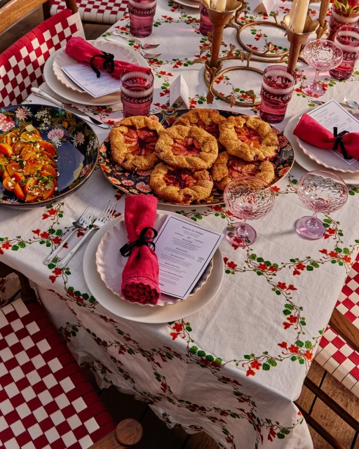 Festive outdoor table setting with pastries, salad, pink glassware, and red-and-white checkered chairs, creating a warm, inviting atmosphere.