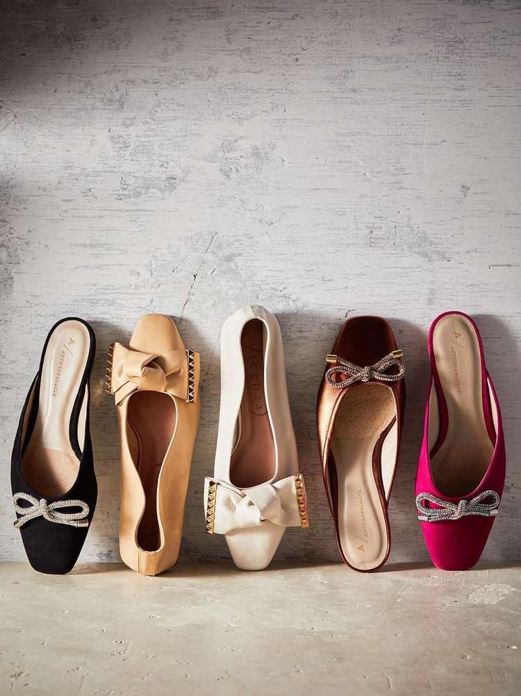 Five elegant ballet flat shoes with decorative bows arranged in a row against a textured off-white backdrop, fashion footwear.