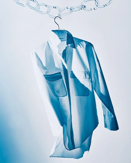 White button-down shirt with pockets hanging from a chain on a hanger against a gradient white and light blue background.