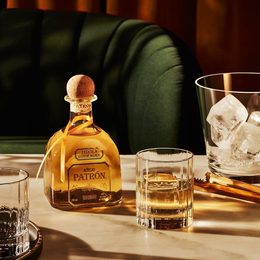 Patron tequila bottle and glasses with ice on a table, presenting an elegant and inviting alcoholic beverage scene.