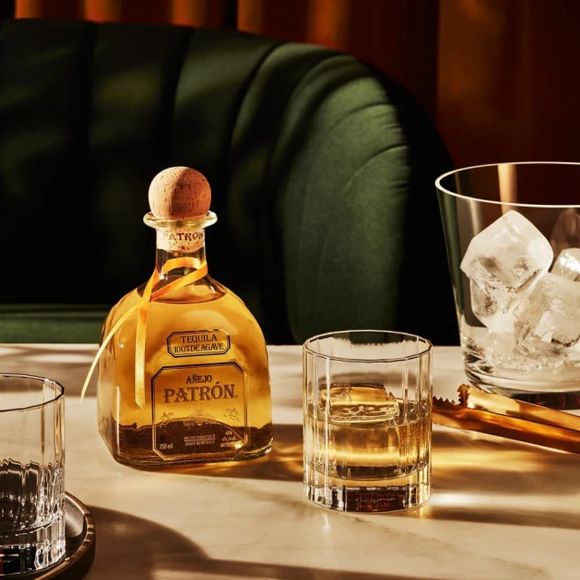 Patron tequila bottle and glasses with ice on a table, presenting an elegant and inviting alcoholic beverage scene.