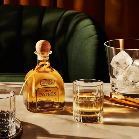 Patron tequila bottle and glasses with ice on a table, presenting an elegant and inviting alcoholic beverage scene.