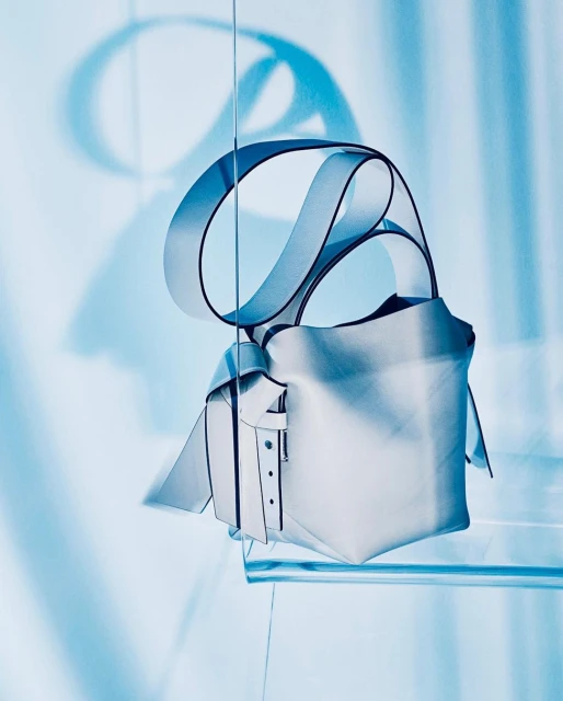 Stylish white leather handbag with black trim and ribbon strap, studio shot against a light blue gradient backdrop with shadow.
