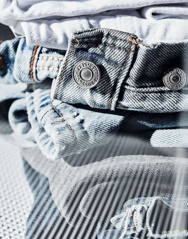 Close-up of folded denim jeans and white t-shirts showing buttons, fabric texture, and casual fashion clothing.