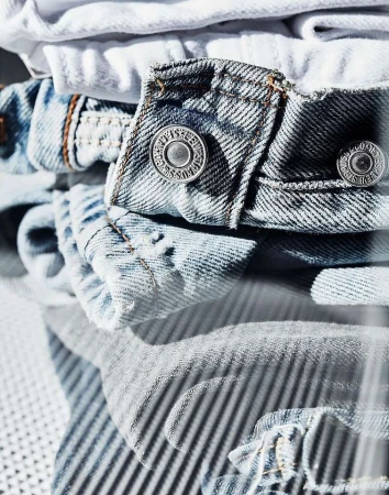 Close-up of folded denim jeans and white t-shirts showing buttons, fabric texture, and casual fashion clothing.