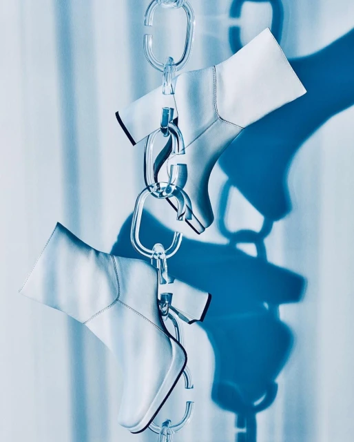 Hanging white leather ankle boots connected by clear acrylic chain links create a surreal, eye-catching high-fashion still life.
