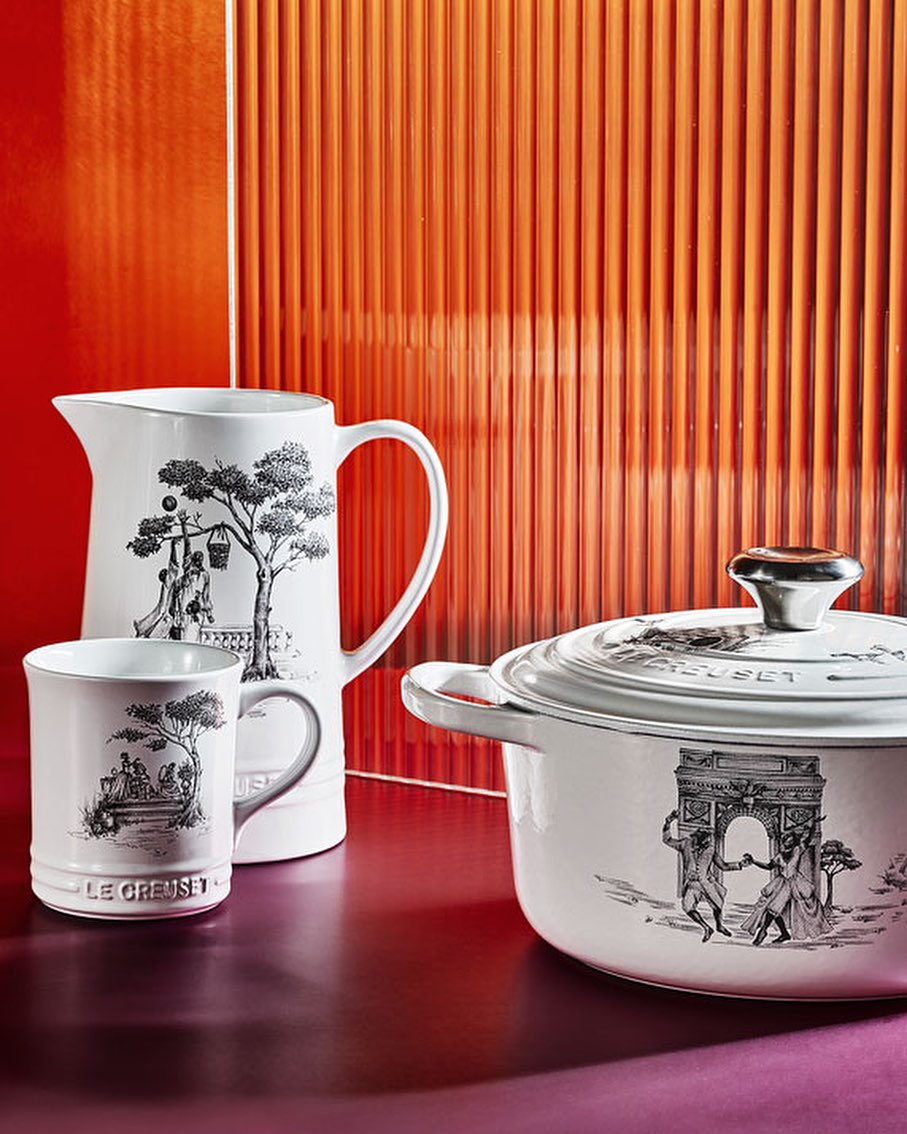 White Le Creuset cookware set featuring a pot with lid, a pitcher, and a mug, all adorned with black and white vintage-style illustrations.