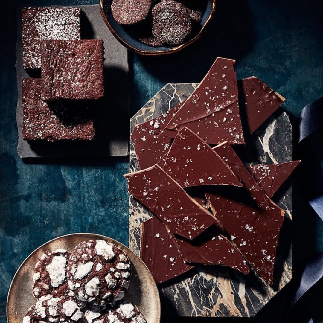 Overhead shot of decadent chocolate brownies, cookies, and bark sprinkled with sugar and salt on marble and slate serving boards.
