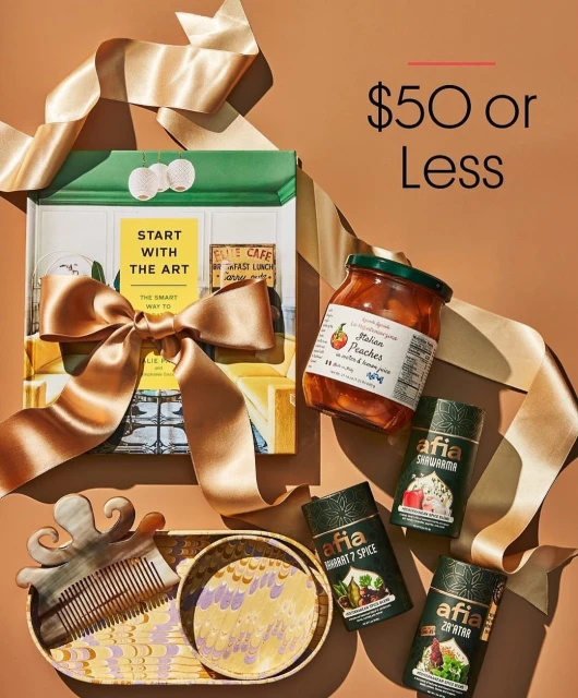Still life shot of a gift set featuring a book, a jar of peaches, hair comb, decorative dishes, and spice containers on a brown background.