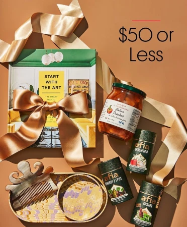 Still life shot of a gift set featuring a book, a jar of peaches, hair comb, decorative dishes, and spice containers on a brown background.