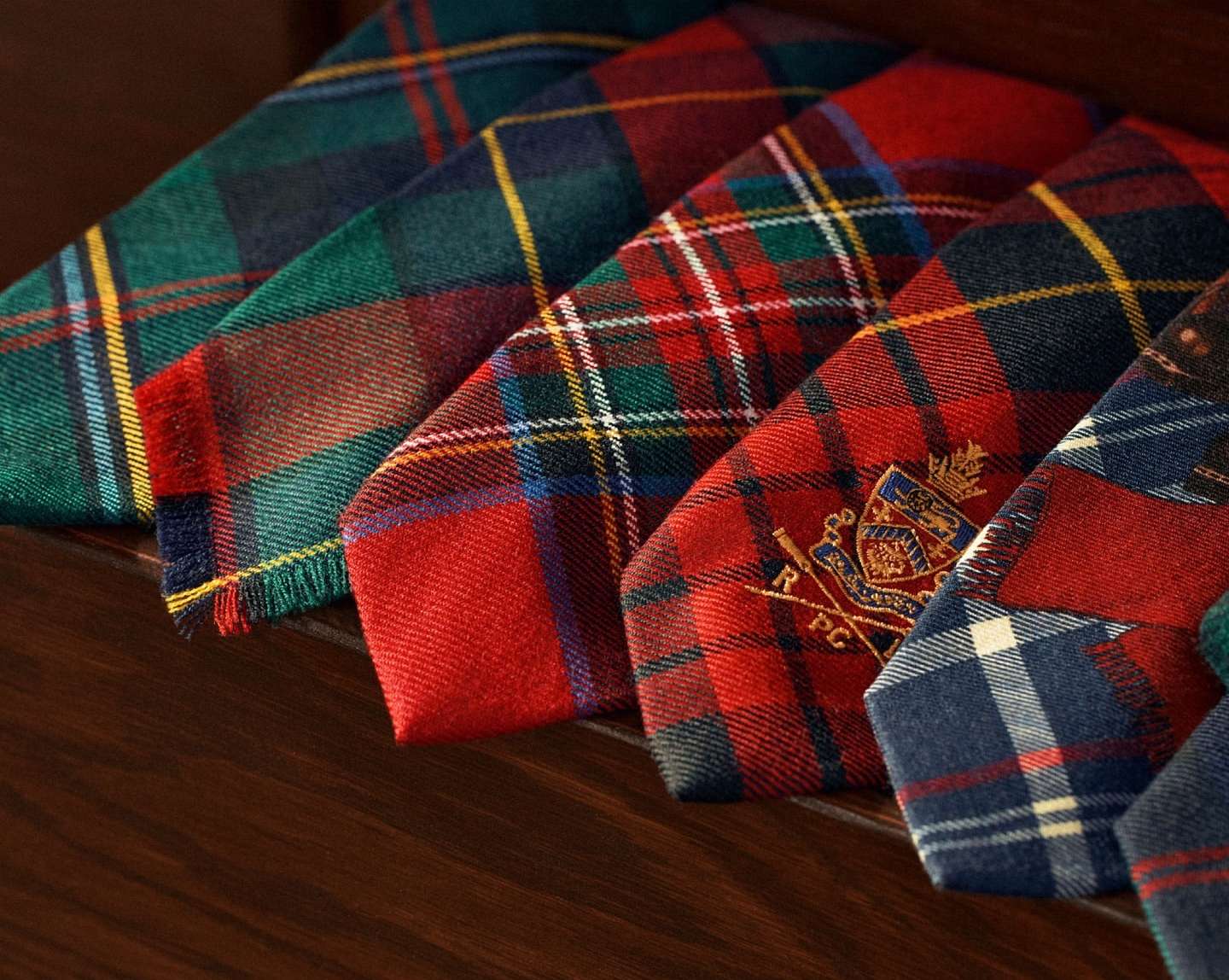 Assortment of colorful plaid ties in green, red, and blue hues, arranged on a dark wooden surface for a classic fashion display.