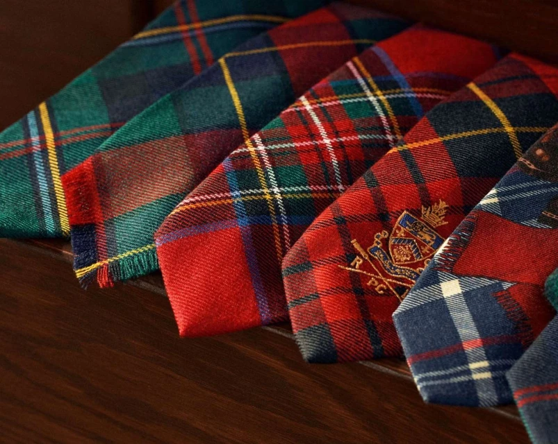Assortment of colorful plaid ties in green, red, and blue hues, arranged on a dark wooden surface for a classic fashion display.